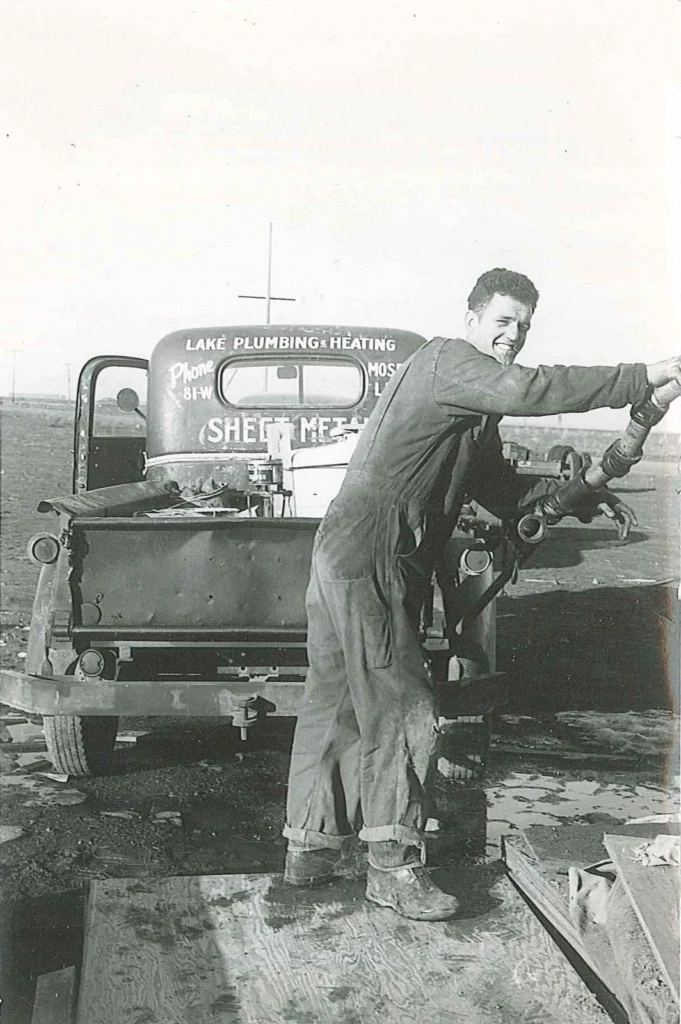 A Person In Work Clothes Fills A Fuel Tank From A Truck Marked &Quot;Lake Plumbing &Amp; Heating,&Quot; Complete With A Phone Number On The Back. This Outdoor Scene, Possibly Set At A Construction Site, Offers A Glimpse Into What We'Re All About—Reliable Service And Expertise Right Where You Need It.