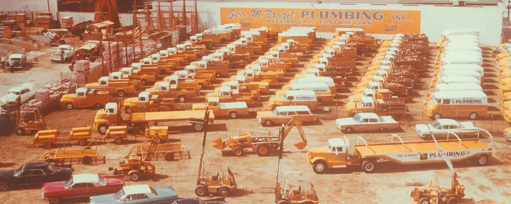 Aerial View From The &Quot;About Us&Quot; Section Shows A Plumbing Company Lot Bustling With Rows Of Yellow Trucks And Vehicles, Ready To Serve.